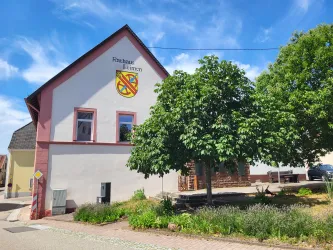 Ein Rathaus mit dem Wappen der Gemeinde befindet sich in einer ruhigen Straße. Umgeben von einem grünen Baum und bunten Blumen.