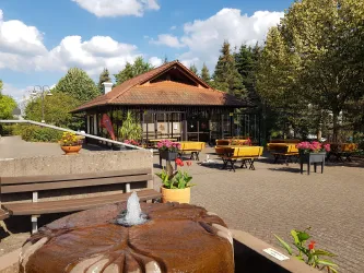 Ein schöner Park mit einem Brunnen im Vordergrund. Im Hintergrund steht ein Gebäude, umgeben von Bäumen und bunten Blumen.
