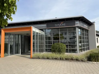 Ein modernes Café mit einer Auswahl an frischen Backwaren und Kaffee. Die Einrichtung ist freundlich und einladend, mit dekorativen Blumen.
