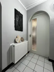 Ein moderner Flur mit grauen Wänden und einem runden Türbogen. Auf dem Heizkörper stehen dekorative Elemente aus Holz.