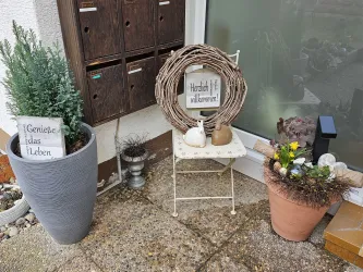 Ein einladender Eingangsbereich mit Pflanzen und Dekoration. Eine kleine Bank trägt einen Willkommenskranz.