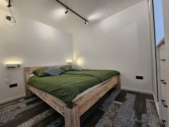 Ein modernes Schlafzimmer mit einem Holzbett. Die Wände sind hell und die Beleuchtung sorgt für eine angenehme Atmosphäre.