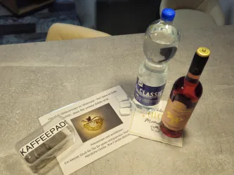 Eine Willkommensnachricht liegt auf einem Tisch neben einem Fläschchen Wasser, einem Fläschchen Wein und Kaffeepads.
