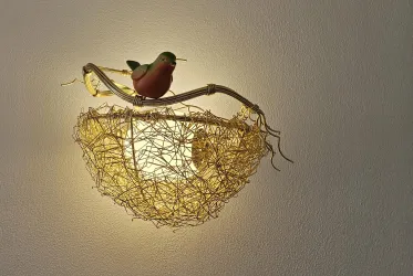 Eine kreative Lampe in Form eines Vogelnests mit einem bunten Vogel auf einem Ast. Das Licht strahlt warm und einladend.