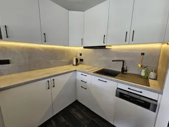 Eine moderne Küche mit weißen Schränken und grauen Arbeitsflächen. Die sanfte Beleuchtung sorgt für eine angenehme Atmosphäre.