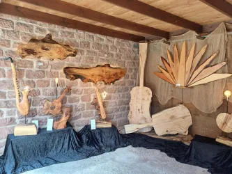 Eine Ausstellung mit Kunstwerken aus Holz, darunter Gitarren und dekorative Stücke. Die Objekte sind auf einem Schwarzen Tuch drapiert und vor einer Steinwand präsentiert.