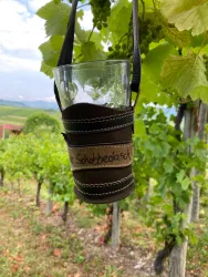 Ein Glas in einer halterung hängt zwischen Weinreben. Im Hintergrund sind sanfte Hügel zu sehen.