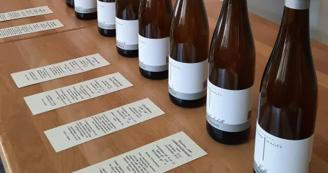 Eine Reihe von Weinflaschen auf einem Holztisch. Daneben liegen beschriftete Menükarten.