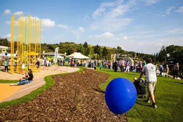 Eine lebhafte Veranstaltung im Freien mit vielen Menschen auf einer Wiese. Im Hintergrund sind gelbe Skulpturen und ein blauer Ball sichtbar.