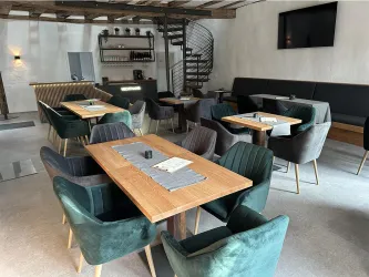 Ein modernes Restaurant mit grauen und grünen Stühlen sowie Holztischen. Im Hintergrund gibt es eine spiralförmige Treppe und eine Bar.