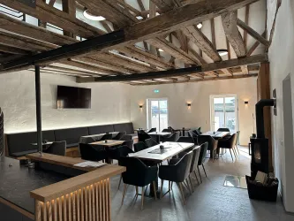 Ein modernes Restaurant mit Holzbalkendecke und stilvollem Interieur. Die Tische sind elegant gedeckt und die Atmosphäre ist einladend.