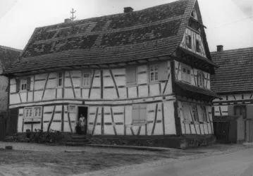 Ein historisches Fachwerkhaus mit einem schrägen Dach und traditioneller Holzverzierung. Es steht in einer ländlichen Umgebung und zeigt die Architektur vergangener Zeiten.
