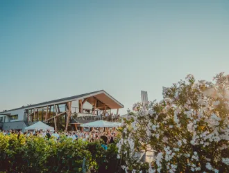 Eine moderne Veranstaltungslocation unter klarem Himmel. Blumen und Menschen im Vordergrund schaffen eine einladende Atmosphäre.