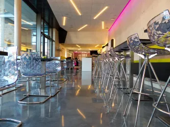 Ein modernes Café mit transparenten Barhockern und einem glänzenden Boden. Die Wände sind hell, und es gibt eine angenehme Beleuchtung.