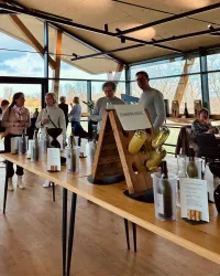 Eine Gruppe von Menschen steht an einem langen Tisch in einem modern gestalteten Raum. Auf dem Tisch befinden sich verschiedene Flaschen und Informationsmaterialien.