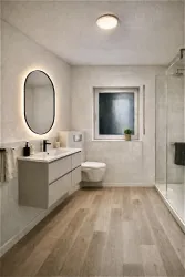 Ein modernes Bad mit hellen Wänden und einem großen Spiegel. Die Dusche ist durch eine Glaswand abgetrennt und es gibt einen kleinen Fenster mit Pflanzen.