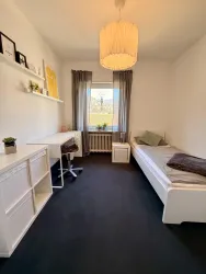 Ein modernes Schlafzimmer mit einem Bett, einem Schreibtisch und einer gemütlichen Lampe. Große Fenster sorgen für viel Licht und einen Blick nach außen.