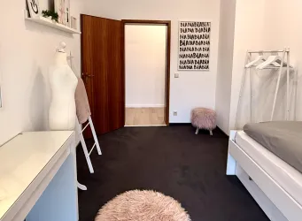 Ein modernes Schlafzimmer mit einem Bett, einem Spiegel und einer weißen Kommode. Der Raum ist hell und minimalistisch eingerichtet, mit einem weichen Teppich und dekorativen Elementen.