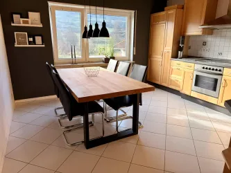 Ein modernes Esszimmer mit einem großen Holztisch und schwarzen Stühlen. Helle Wände und ein Fenster bieten viel Tageslicht.