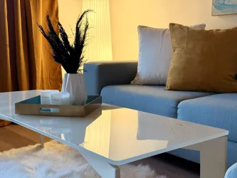 Ein stilvolles Wohnzimmer mit einem blauen Sofa und einem modernen Couchtisch. Der Tisch ist mit einer dekorativen Schale und einer Vase mit Pflanzen geschmückt.