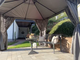 Ein gemütlicher Pavillon mit einer Bank und einem Tisch. Die Umgebung ist grün und gepflegt.
