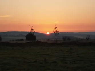 Ein wunderschöner Sonnenaufgang über hügeliger Landschaft. Sanfte Farben erhellen den Himmel und verleihen der Szene eine friedliche Atmosphäre.