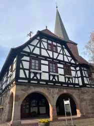 Ein historisches Fachwerkhaus mit einer markanten Steeple und schönen Fenstern. Es befindet sich in einer malerischen Umgebung mit Blumen vor dem Eingang.