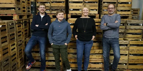 Eine Gruppe von vier Personen steht vor Holzregalen. Sie lächeln freundlich und wirken entspannt.