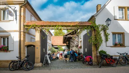 Eine belebte Gasse mit einem Torbogen und vielen Menschen. Freizeitangebote mit Fahrrädern sind sichtbar, umgeben von charmanten Gebäuden.