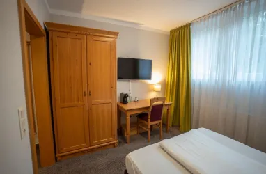 <p>Einzelzimmer im Hotel Annaberg Blick vom Bett auf einen Schreibtisch, Schrank und Fernseher</p>