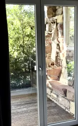 Ein Fenster mit Blick auf eine sichere Holzterrasse und eine grüne Umgebung. Die Wände sind aus Steinen und es gibt eine gemütliche Bank.