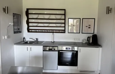 Eine moderne Küche mit weißen Schränken und einem grauen Arbeitsbereich. An der Wand hängen Kunstwerke und Geschirr ist auf einem Regal präsentiert.