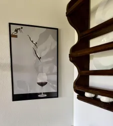 Ein gerahmtes Kunstwerk zeigt drei Taucher, die ins Wasser springen, vor einem großen Weinglas. Im Hintergrund ist ein Holzregal mit Geschirr zu sehen.