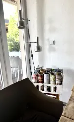 Eine gemütliche Leseecke mit einem modernen Lampen und einem Regal voller Zeitschriften. Die große Fensterscheibe lässt viel Licht herein und bietet einen Blick nach draußen.