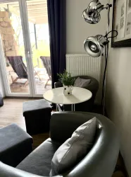 Eine moderne Sitzecke mit zwei grauen Sesseln und einem kleinen Tisch. Auf dem Tisch steht eine Vase mit einer Pflanze und im Hintergrund sind große Fenster mit Blick nach draußen.