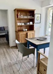 Ein helles, modern eingerichtetes Esszimmer mit einem Holzschrank und einem Tisch in Blau. Es gibt eine gemütliche Atmosphäre mit Stühlen und Geschirr auf dem Tisch.