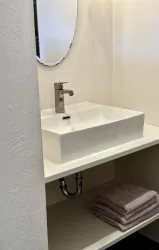 Ein modernes Waschbecken mit einem eleganten Wasserhahn. Darunter liegen graue Handtücher auf einem Regal.