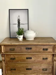 Ein Holztisch mit drei Schubladen, auf dem eine weiße Teekanne und ein kleiner Krug stehen. Dahinter hängt ein schwarz-weißes Bild einer Person in sportlicher Pose.