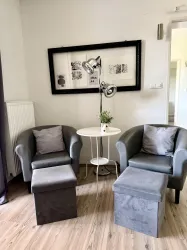 Ein gemütlicher Wohnbereich mit zwei grauen Sessel und einem kleinen Tisch. Eine Stehlampe und ein dekoratives Element in der Mitte schaffen eine einladende Atmosphäre.