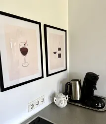 Zwei gerahmte Bilder mit Getränkeillustrationen hängen an der Wand. Auf der Küchentheke steht eine Kaffeemaschine und ein Teekännchen.