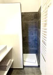 Ein modernes Badezimmer mit eleganten, dunkelgrauen Fliesen. Die Dusche ist einfach und funktional, mit einem Handtuch auf dem Boden.