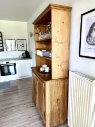 Ein hölzernes Sideboard mit Gläsern und Geschirr auf den Regalen. Im Hintergrund ist eine moderne Küche sichtbar.