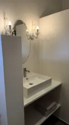 Ein modernes Badezimmer mit einem weißen Waschbecken und einem runden Spiegel. An der Wand sind zwei elegante Leuchten angebracht.