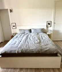 Ein einfaches Schlafzimmer mit einem großen, einladenden Bett. Die Wände sind hell, und es gibt einige dekorative Bilder neben dem Bett.