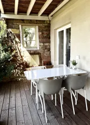 Ein gemütlicher Balkon mit einem weißen Tisch und grauen Stühlen. Die Wand ist aus Steinen und das Licht fällt schön durch das Fenster.