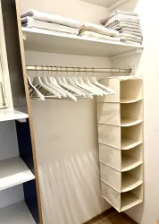 Ein ordentlicher Kleiderschrank mit aufgerollten Handtüchern und einem Kleiderständer. Auf der rechten Seite befindet sich ein praktischer Organizer mit mehreren Fächern.