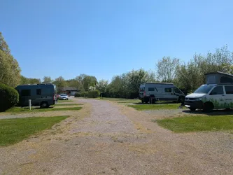 Ein Campingplatz mit mehreren Wohnmobilen und viel grünem Gras. Der Himmel ist klar und blau, ideal für einen Outdoor-Urlaub.