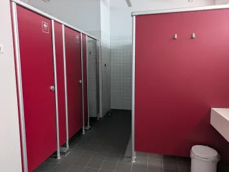 Ein Badezimmer mit roten Trennwänden und einem Waschbecken. Der Boden ist grau gefliest und es gibt einen Mülleimer.