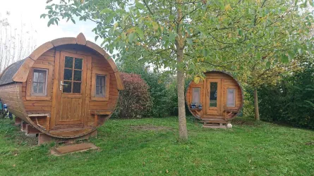 Zwei runde Holzhäuser stehen in einem grünen Garten. Umgeben von Bäumen bietet die Szene eine gemütliche und naturnahe Atmosphäre.