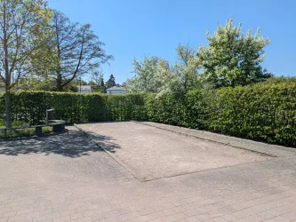 Ein leerer Platz umgeben von Büschen und Bäumen. Der Himmel ist klar und blau.